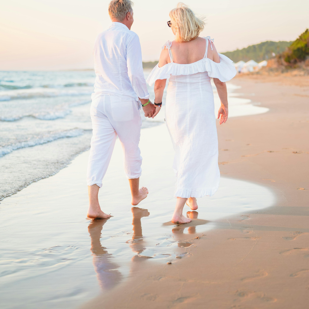 couple dressed in white walking hand in hand along a beach